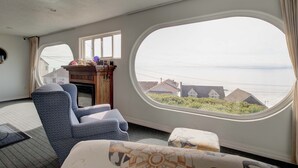 Een kamer met een groot rondboogvenster, een open haard en twee fauteuils.