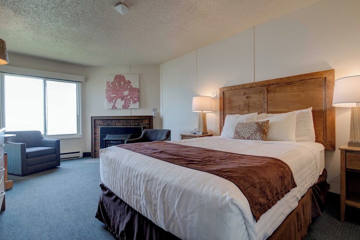 A hotel room with a large bed, a fireplace, a desk, and a chair.