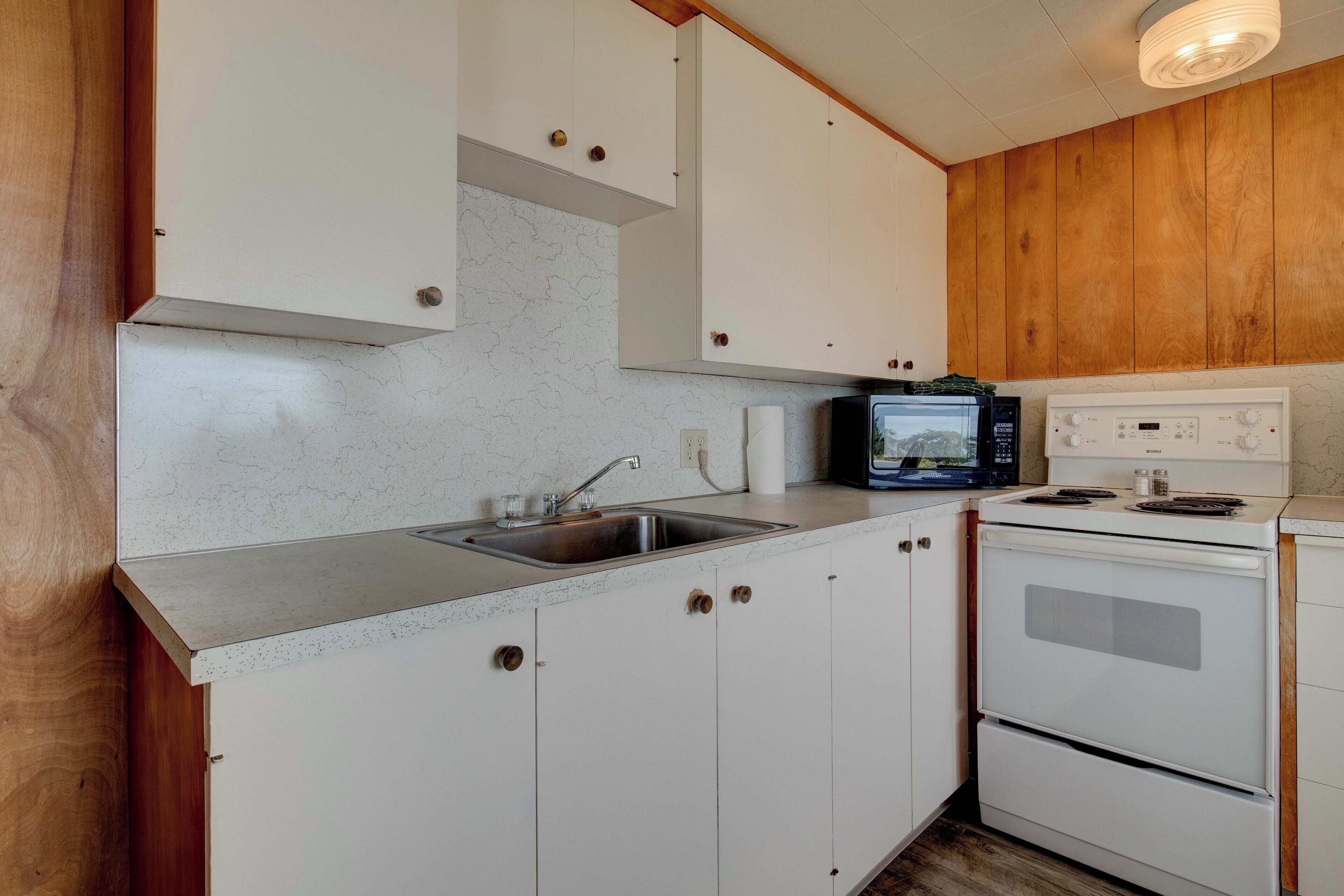 Una cocina con gabinetes blancos, un lavamanos de acero inoxidable, un microondas y una estufa.