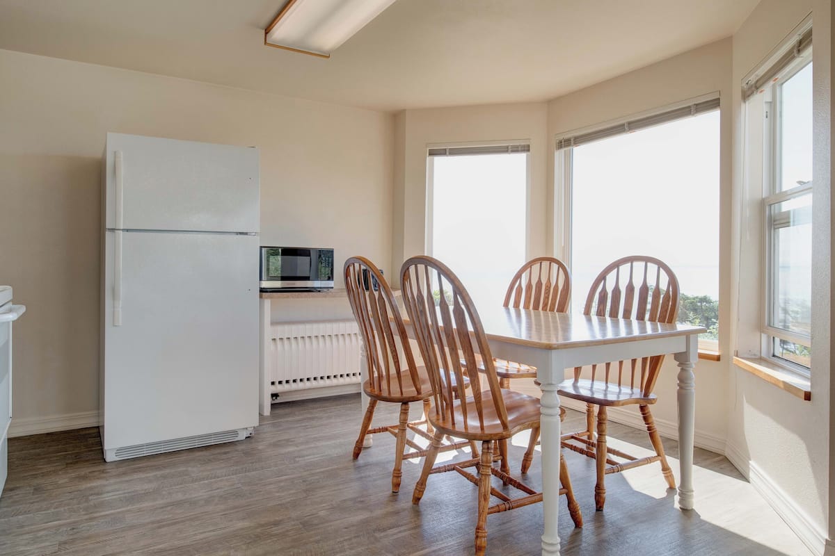 A dining area with a white table and wooden chairs, a white refrigerator, and a microwave on a white cabinet.