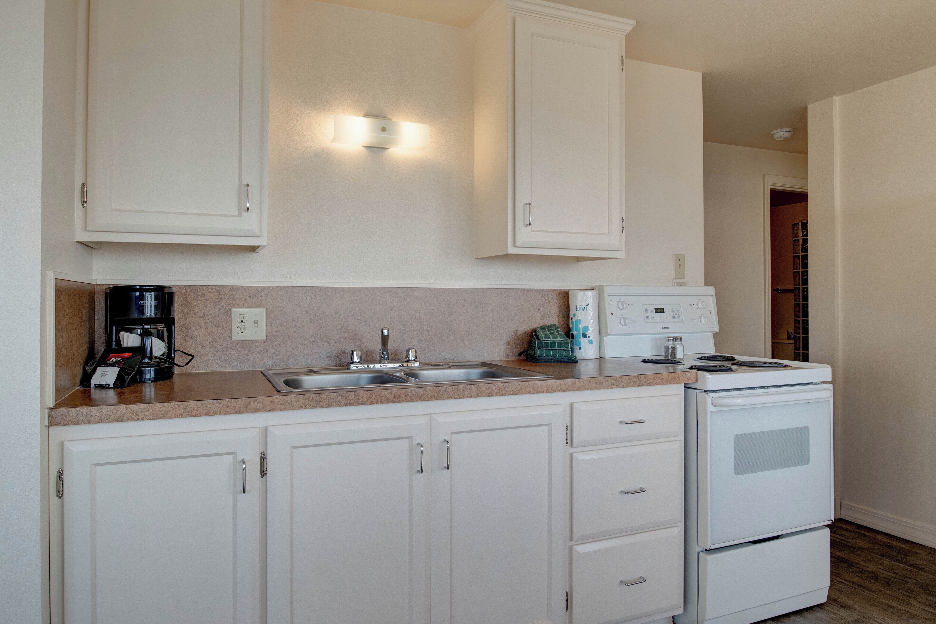 A kitchen with white cabinets, a double sink, a coffee maker, a toaster, and a stove.