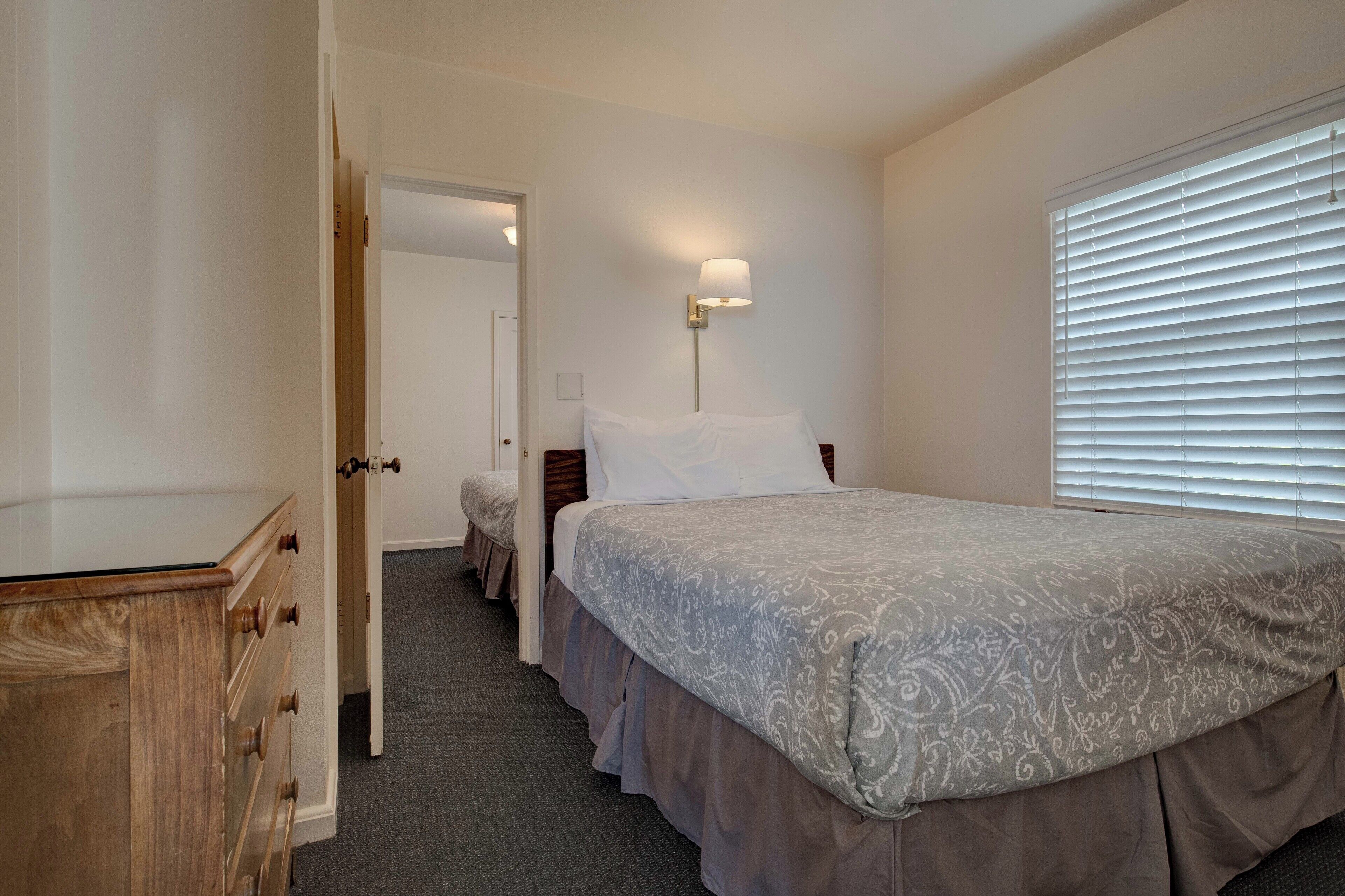 A bedroom with a bed, a nightstand, a lamp, and a window with blinds.