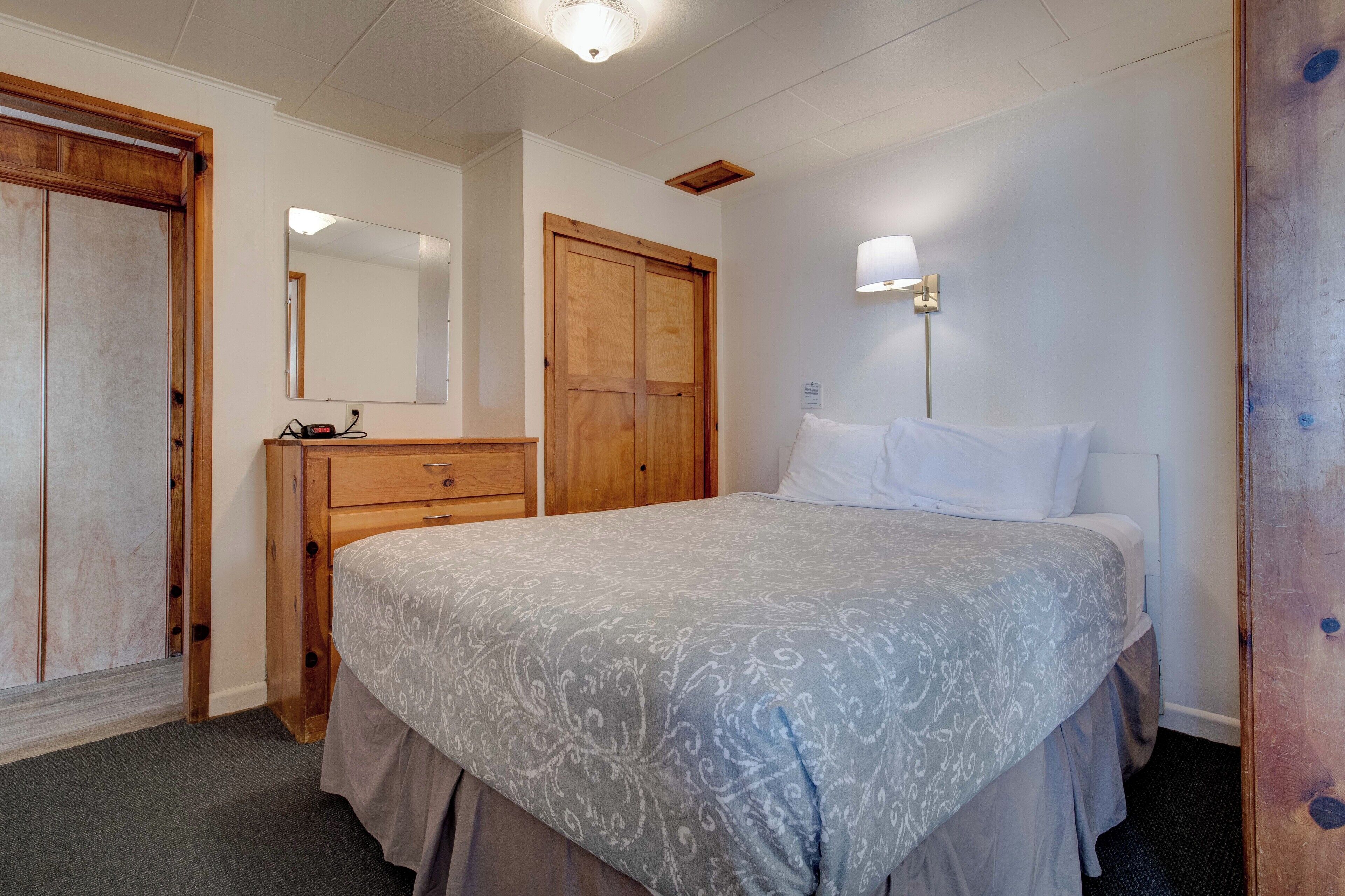 Un dormitorio con una cama, un aparador, un armario de madera, un espejo y una lámpara de pared.