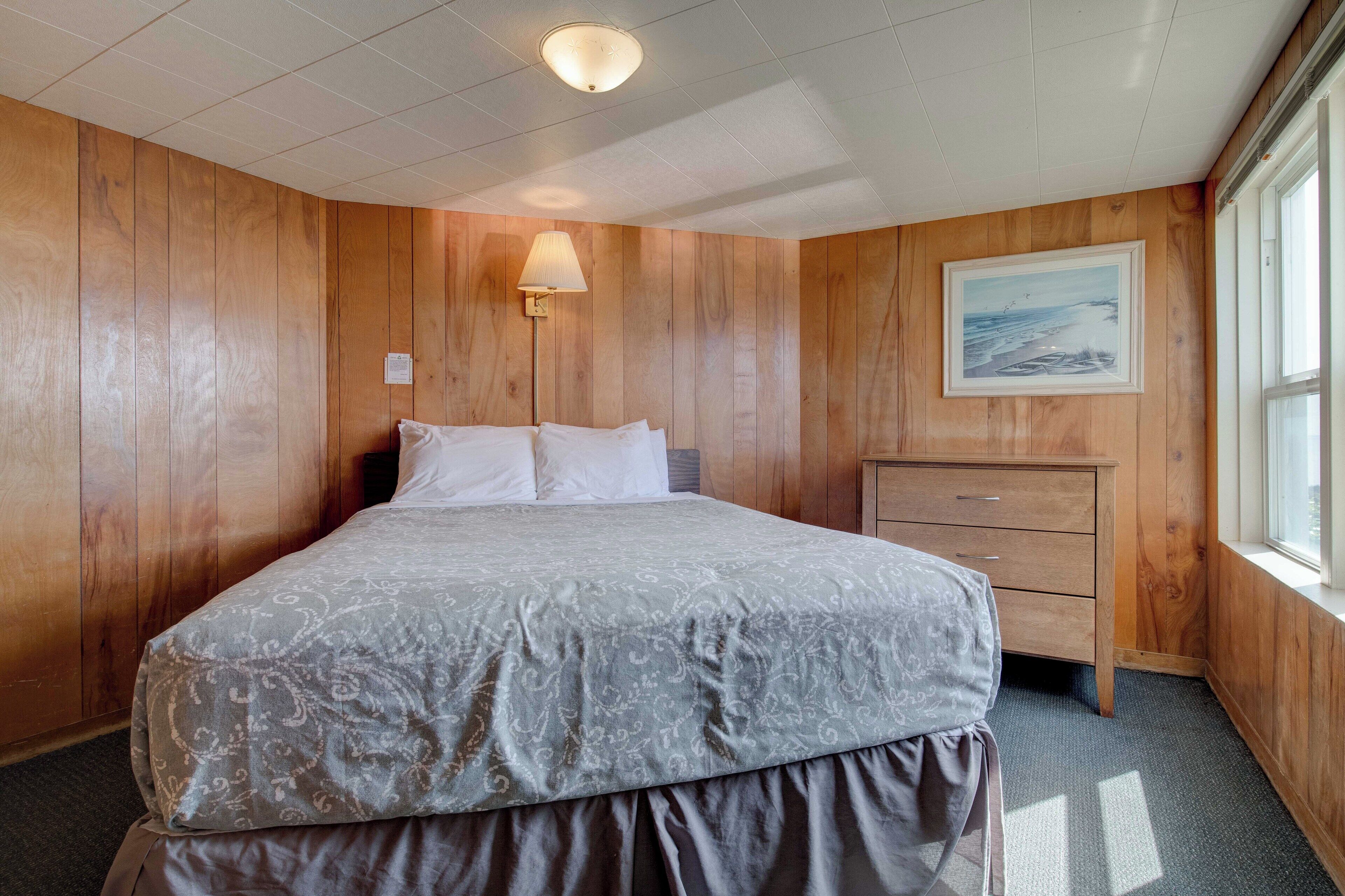 Une chambre à coucher avec un lit, une table de chevet, une commode, un tableau et une fenêtre.
