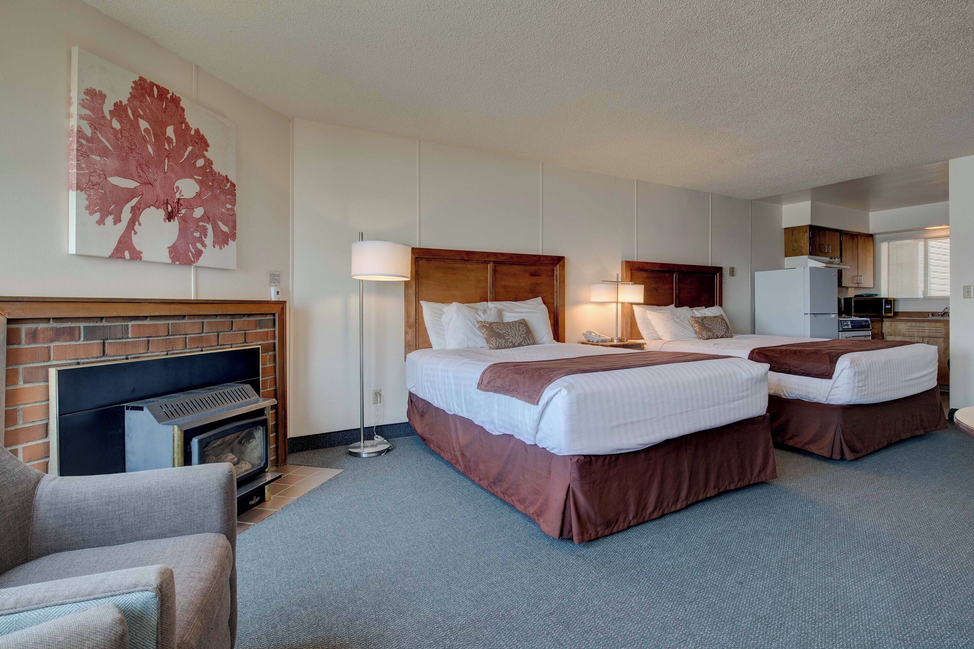 A hotel room with two beds, a fireplace, a kitchenette, and a large window.