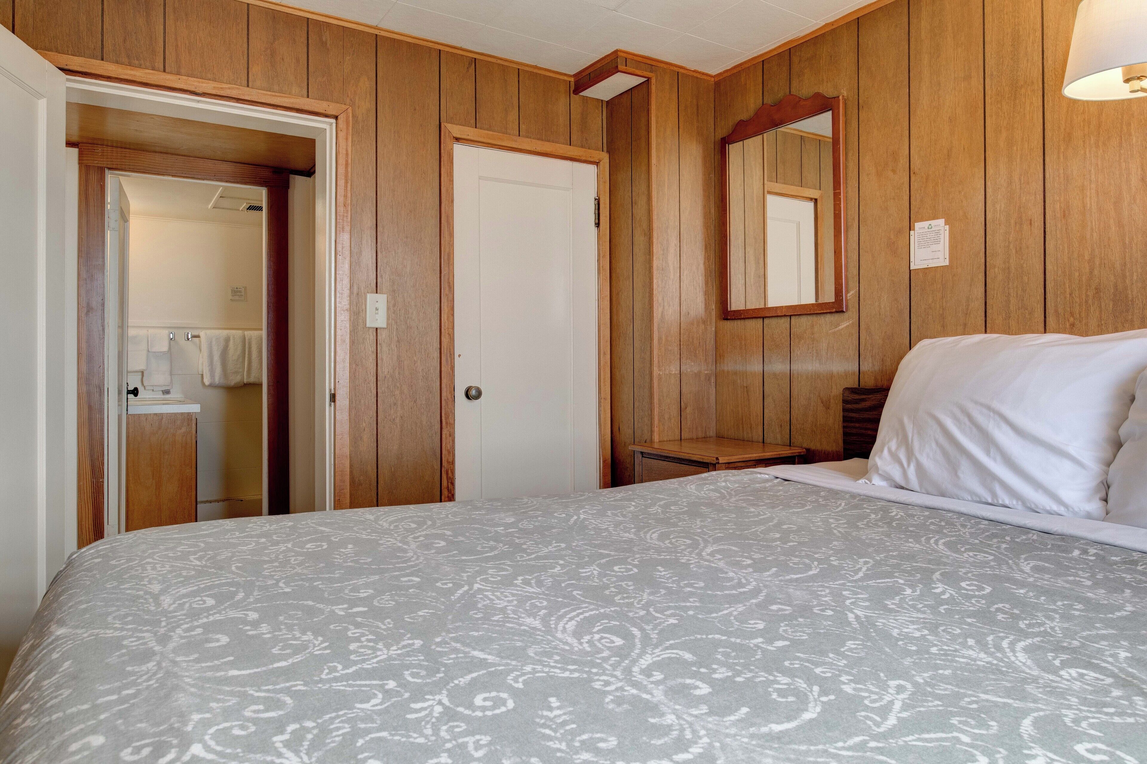 A bedroom with a bed, wooden walls, a door, and a mirror.
