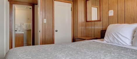 Un dormitorio con cama, paredes de madera, una puerta y un espejo.