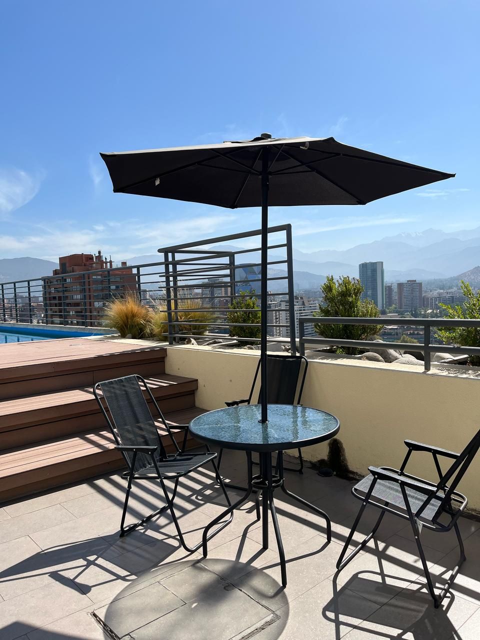 Eine Dachterrasse mit einem Glastisch, Stühlen und einem Sonnenschirm.