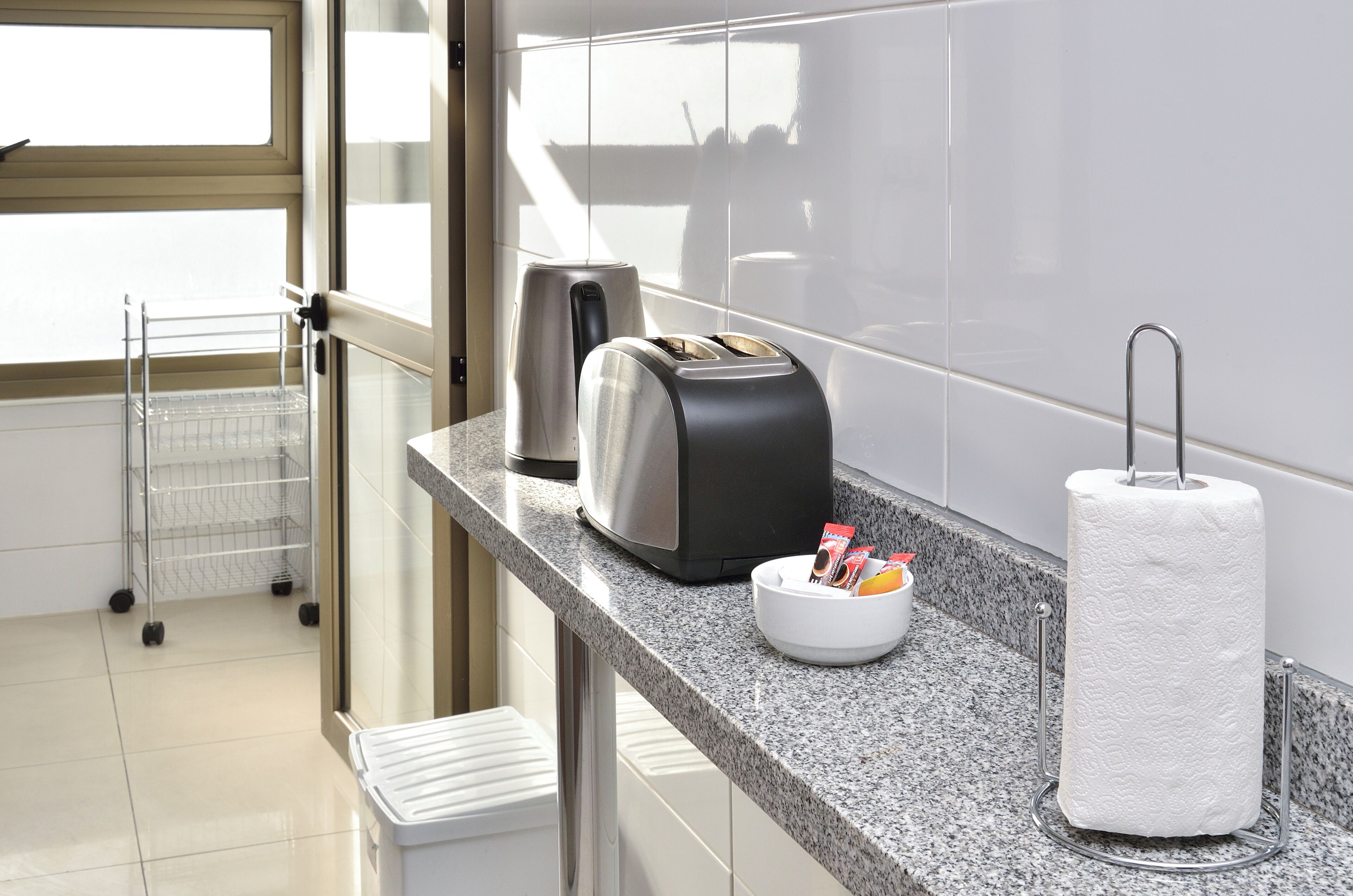 Una cocina moderna con encimera de granito, cafetera, tostadora, dispensador de toallas de papel y un tazón pequeño con objetos.