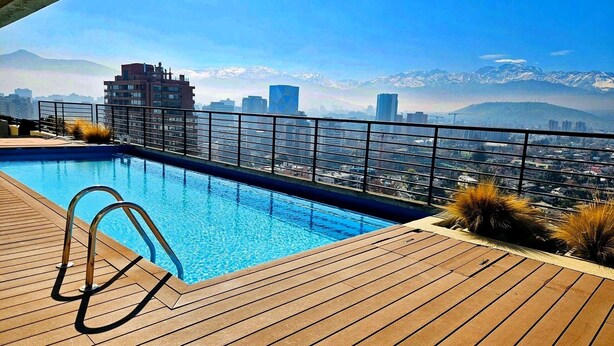 A rooftop pool with a city view, metal railings, and wooden deck.