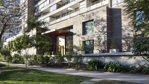 A modern multi-story building with balconies, large windows, and a well-maintained garden area.