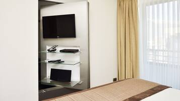 Une chambre d’hôtel équipée d’un lit, d’un téléviseur à écran plat fixé au mur et d’une étagère en verre contenant des appareils électroniques.