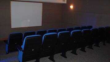 Une salle de cinéma avec des rangées de sièges noirs et bleus, un écran blanc et un projecteur fixé au plafond.