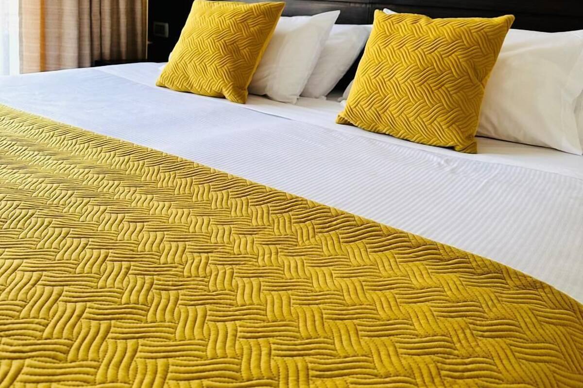 Una habitación de hotel con una cama, dos almohadas, cabecero y una ventana con cortinas.