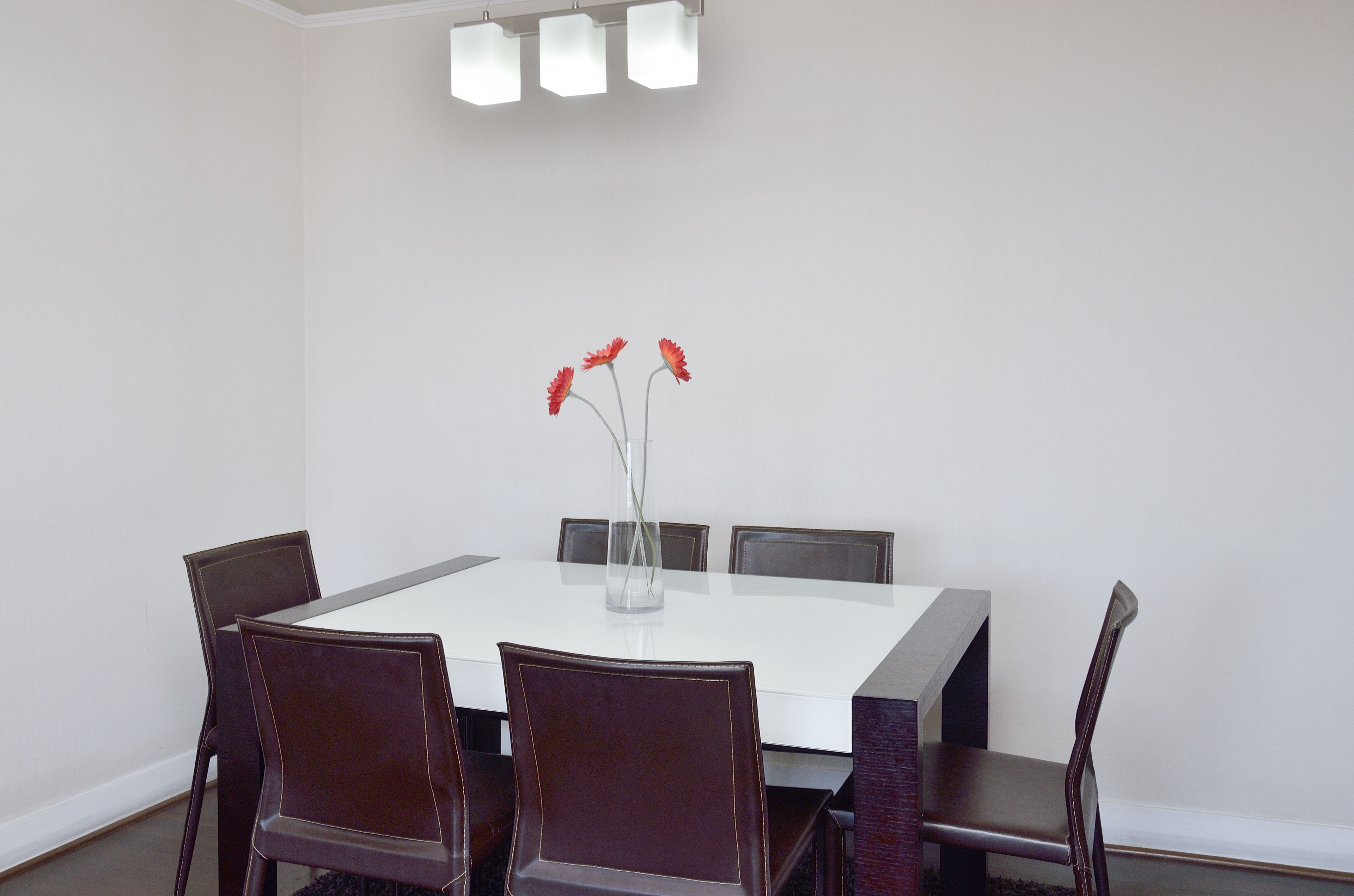 Uma sala de conferências com uma mesa branca, cadeiras escuras e um vaso com flores vermelhas.