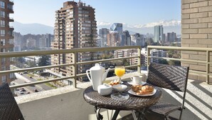 A balcony with breakfast items, wicker chairs, and a cityscape with mountains in the background.