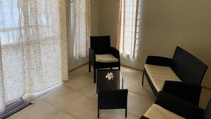 A room with a sofa, a chair, a small table, and patterned curtains. - Tianas Beach (Rarotonga)