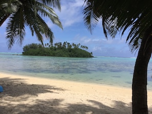 Una playa con agua turquesa cristalina, una orilla arenosa y una pequeña isla con abundante vegetación al fondo.