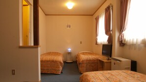 Ein Hotelzimmer mit zwei Betten, einem Schreibtisch mit Computer, einem kleinen Tisch und einem Fenster mit Vorhängen.