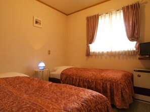A room with two beds, a small table with a lamp, a TV, and a window with curtains.