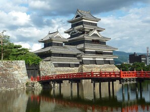 A traditional Japanese castle with multiple tiers, a stone wall, and a red bridge over water.