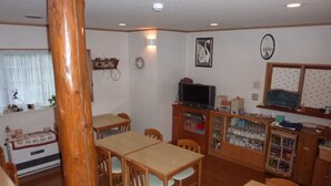 Ein Essbereich mit Holztischen und -stühlen, einem Fernseher auf einem Schrank und einem Kühlschrank mit Glastüren.