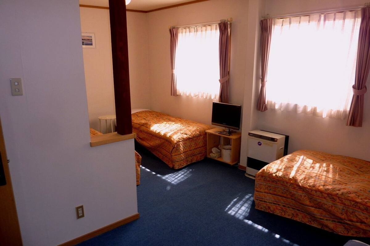 A compact hotel room with two single beds, a television, a small desk, and a window with curtains.