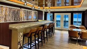 A modern bar area with a long counter, multiple stools, and a view of the sea through large windows. - Lake View Suites (West Yellowstone)