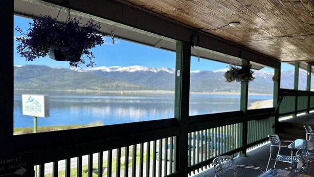 A covered outdoor seating area with a view of a lake and mountains. - Lake View Suites (West Yellowstone)