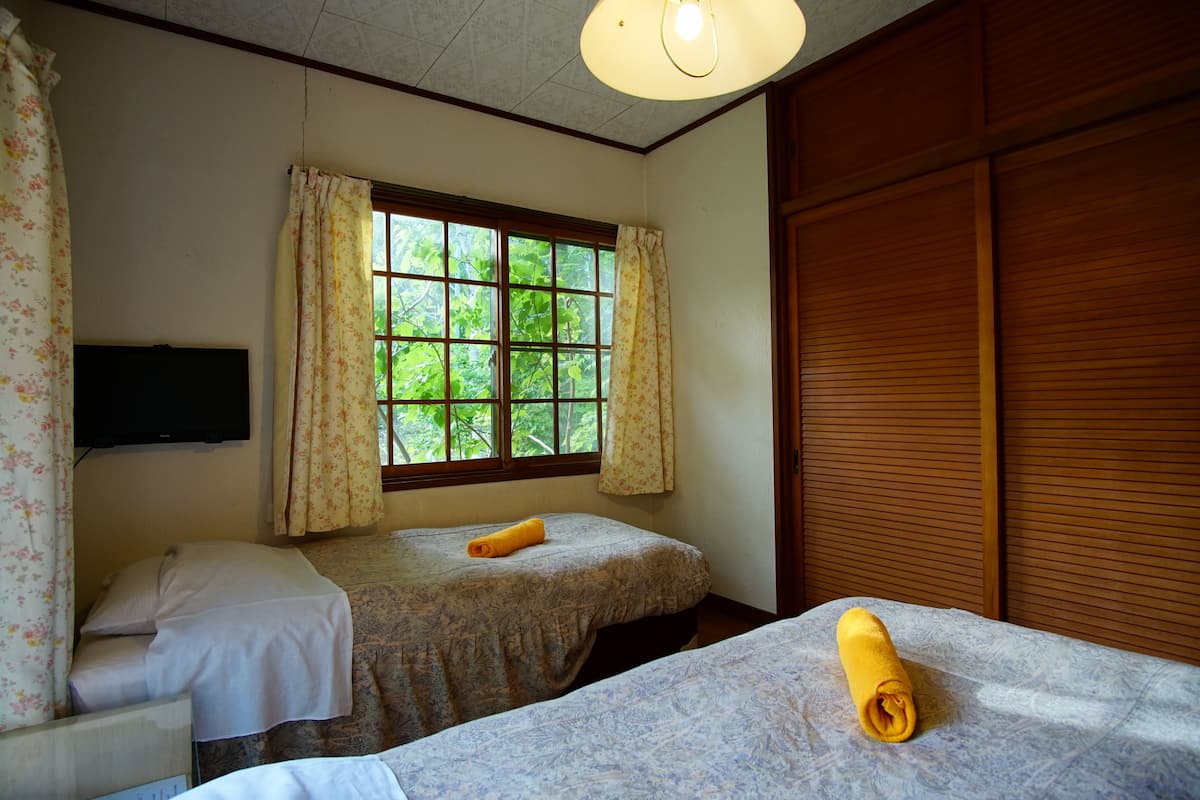A room with two beds, a window with curtains, a flat-screen TV, and wooden paneling.