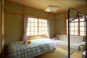 A traditional Japanese-style room with tatami flooring, a futon bed, a low wooden ceiling, and large windows with curtains. - share&guesthouse HAKUBA SHARE - Hostel (Hakuba)