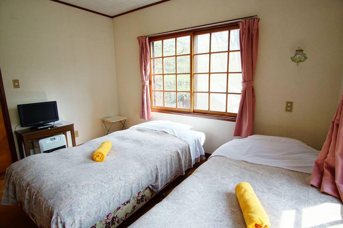A hotel room with two beds, a television on a small table, and a window with curtains.