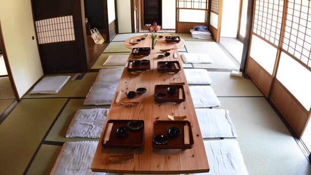 Ein traditioneller japanischer Raum mit Tatami-Bodenbelag, einem Holztisch, der mit Teezeremonie-Gefäßen bestückt ist, und Shoji-Schirmen.
