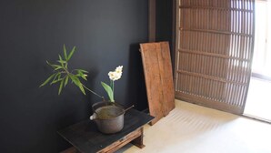 Ein traditioneller japanischer Raum mit Tatami-Boden, schwarzer Wand, einer Holzbank, einem kleinen Tisch mit Topf und Blume sowie einer Schiebetür.