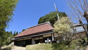 Ein traditionelles japanisches Gebäude mit einem Ziegeldach, umgeben von viel Grün und blauem Himmel.