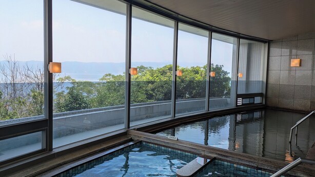 A swimming pool with clear views of the outdoors, including trees and a distant landscape. - Kokuminshukusha Rainbow Sakurajima (Kagoshima)