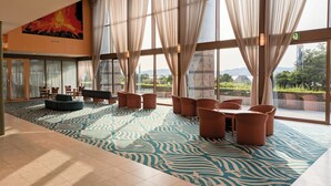 A spacious lobby with a patterned carpet, large windows with curtains, and a seating area with chairs and a sofa. - Kokuminshukusha Rainbow Sakurajima (Kagoshima)
