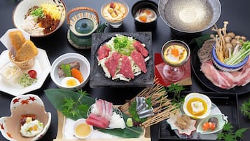 A variety of Japanese dishes including sushi, sashimi, and tempura, arranged on a table with a dark background.