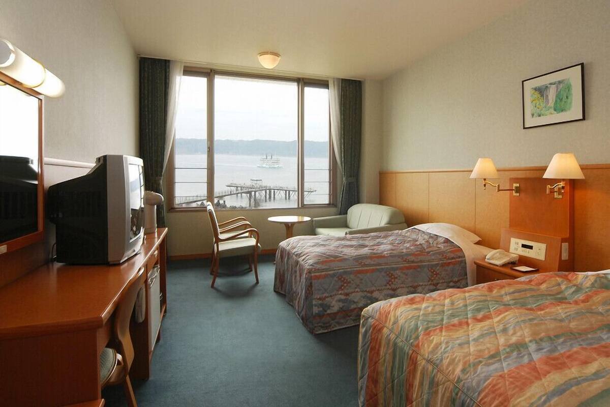 Une chambre d’hôtel avec deux lits, un bureau avec une télévision, une chaise, une petite table et une vue sur l’eau.
