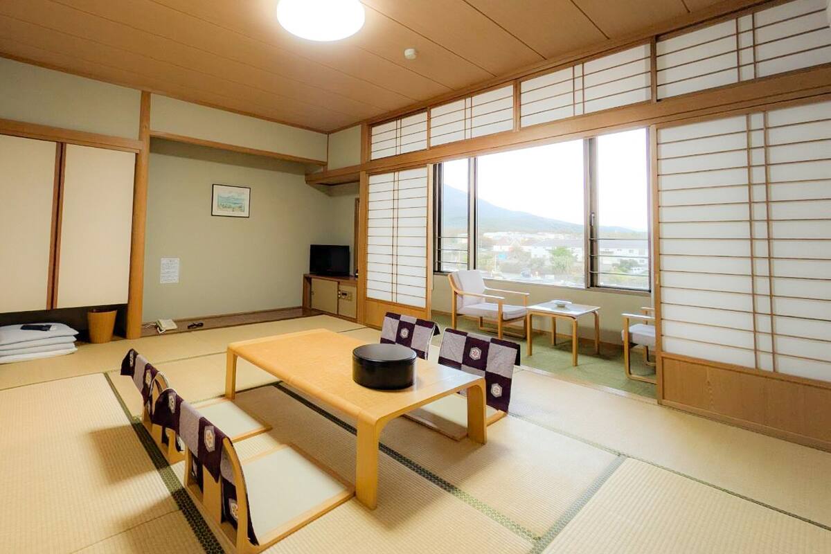 Une pièce de style japonais traditionnel, avec un sol recouvert de tatamis, une table basse avec des coussins, des portes coulissantes et une vue sur l’extérieur.