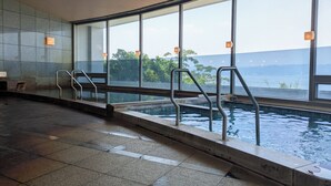 An indoor swimming pool with clear glass walls, metal railings, and a view of a body of water and greenery. - Kokuminshukusha Rainbow Sakurajima (Kagoshima)