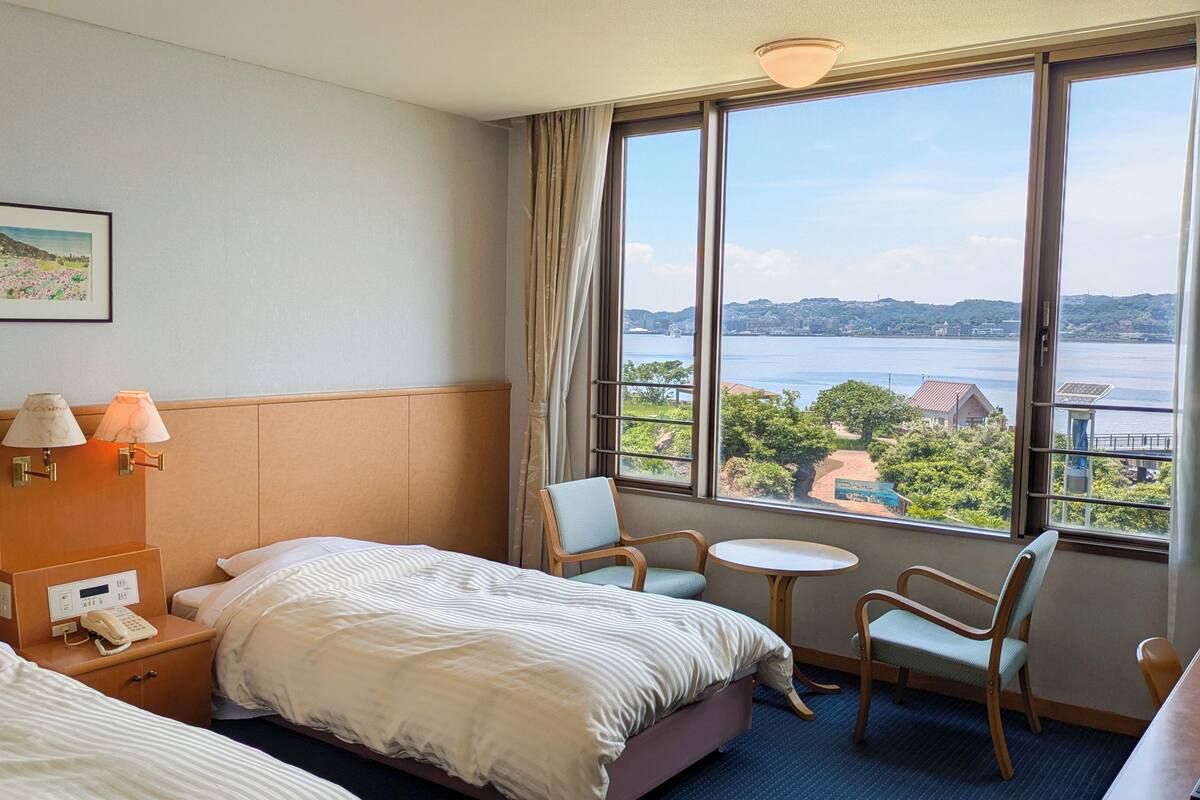 Une chambre d’hôtel avec deux lits, une petite table, une chaise et une vue sur une étendue d’eau.