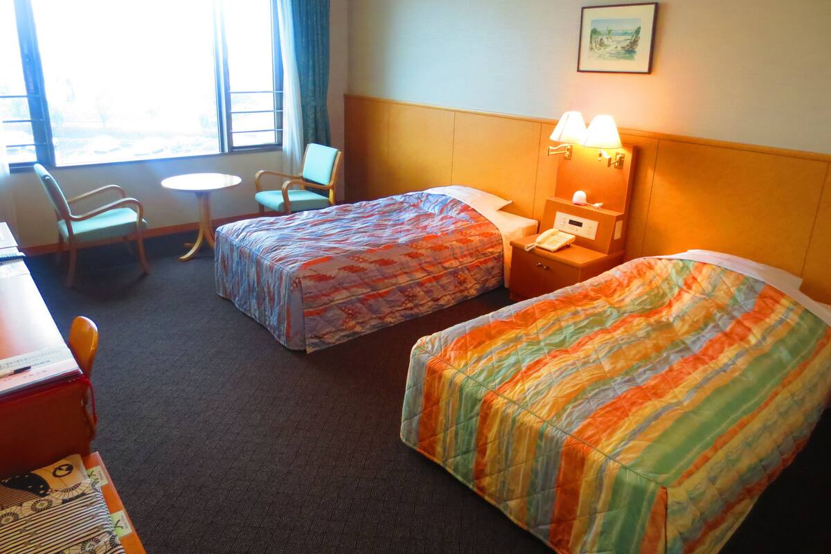 Une chambre d’hôtel avec deux lits, un bureau, une chaise, une petite table et une fenêtre avec des rideaux.