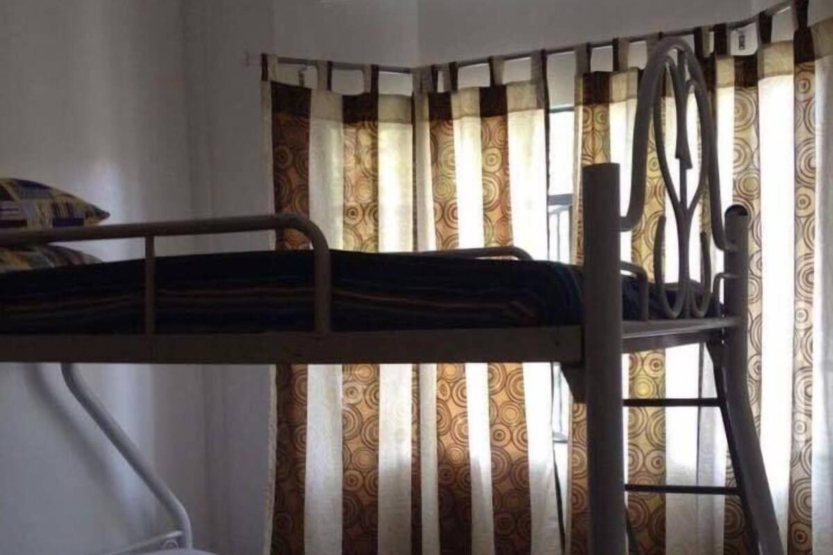 Une chambre avec un lit superposé, des rideaux à motifs et une structure en métal.