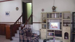 A living room with a plaid sofa, a television on a stand, a staircase, and a bookshelf. - Kensington Garden BNB (Baguio)