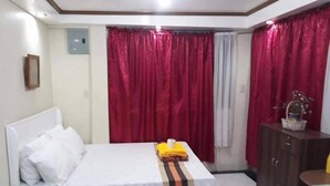 A room with a bed, a small table, and a cabinet. - Kensington Garden BNB (Baguio)