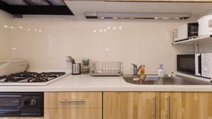 A modern kitchen with wooden cabinets, a stainless steel sink, a built-in oven, and a microwave. - Kokoro House (Osaka)