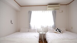 A room with two beds, a small table, and an air conditioning unit. - Kokoro House (Osaka)