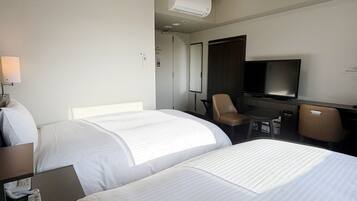 A hotel room with two beds, a desk with a telephone, a chair, a television, and an air conditioning unit.