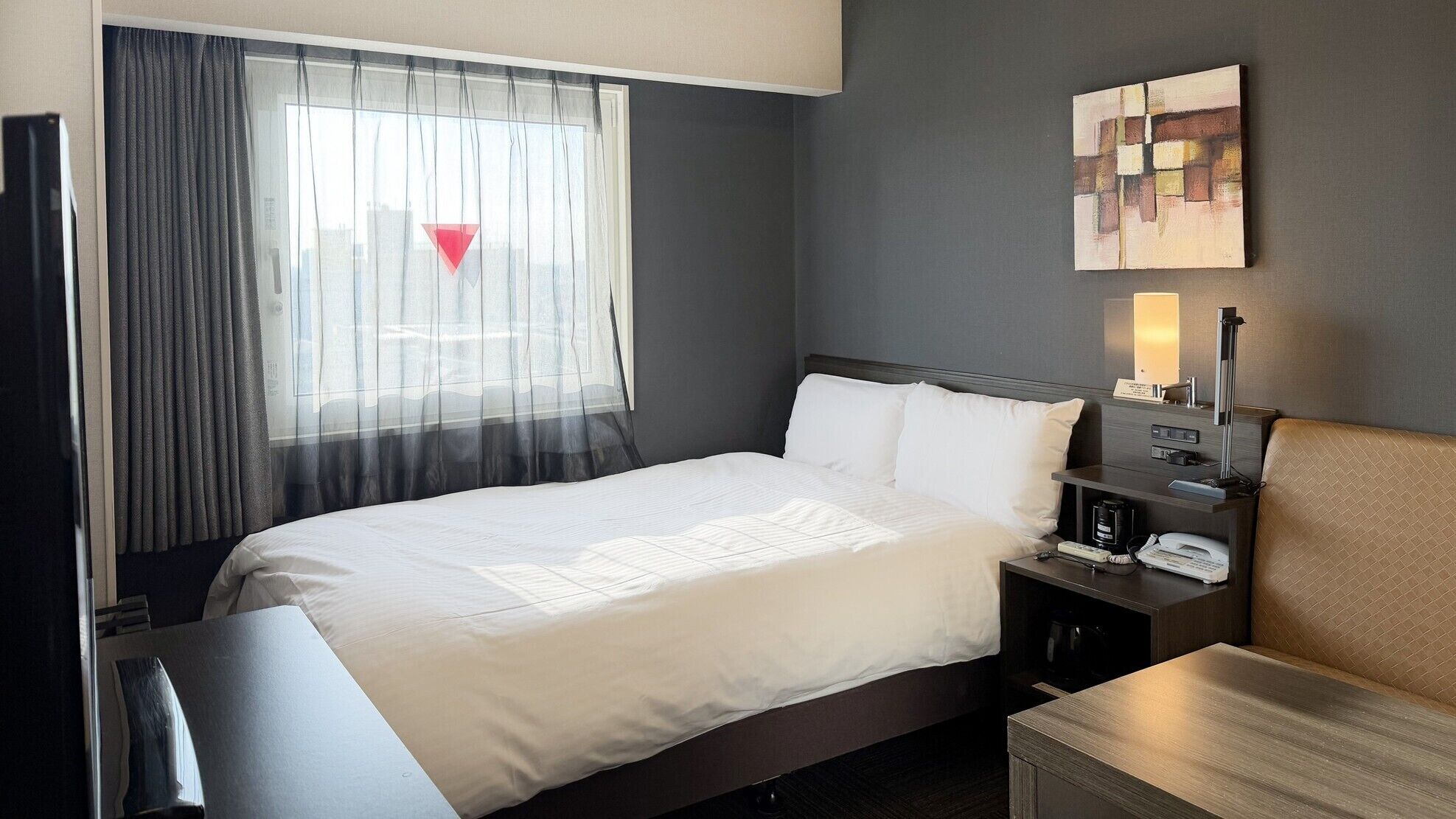 A hotel room with a bed, bedside table, lamp, and artwork on the wall.